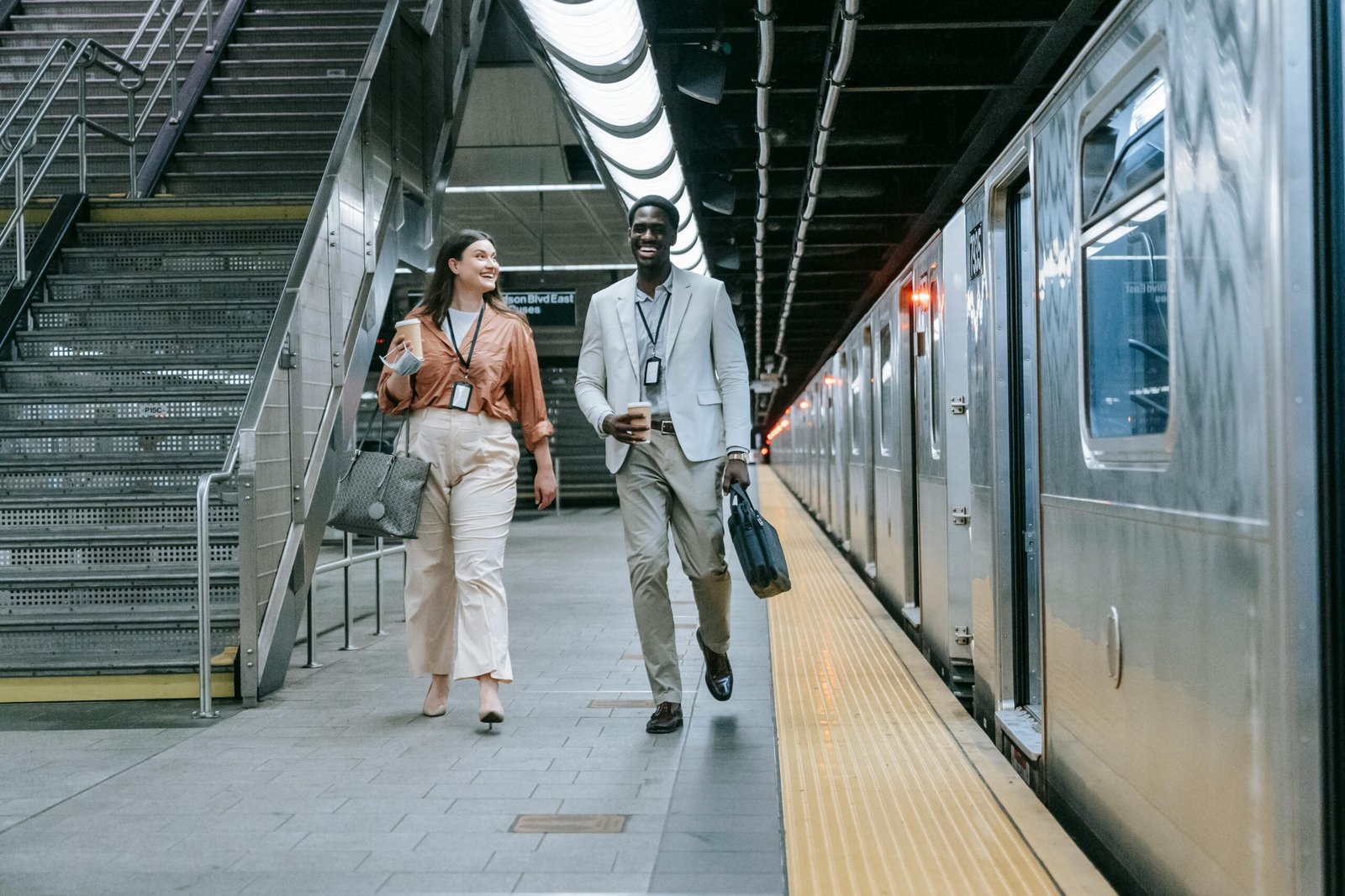 Two colleagues walking and chatting joyfully at a bustling subway station.